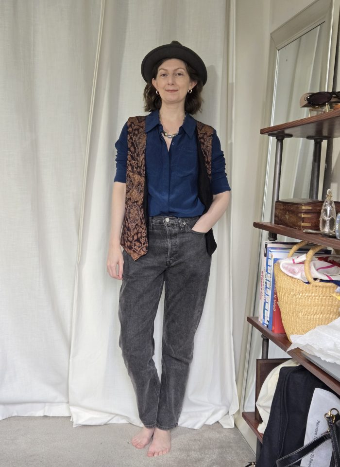 navy button down shirt, black jeans, patterned vest with fedora