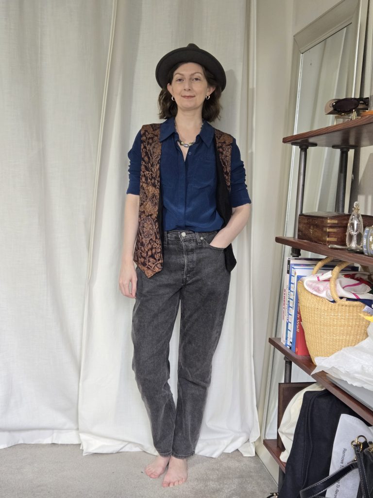 navy button down shirt, black jeans, patterned vest with fedora