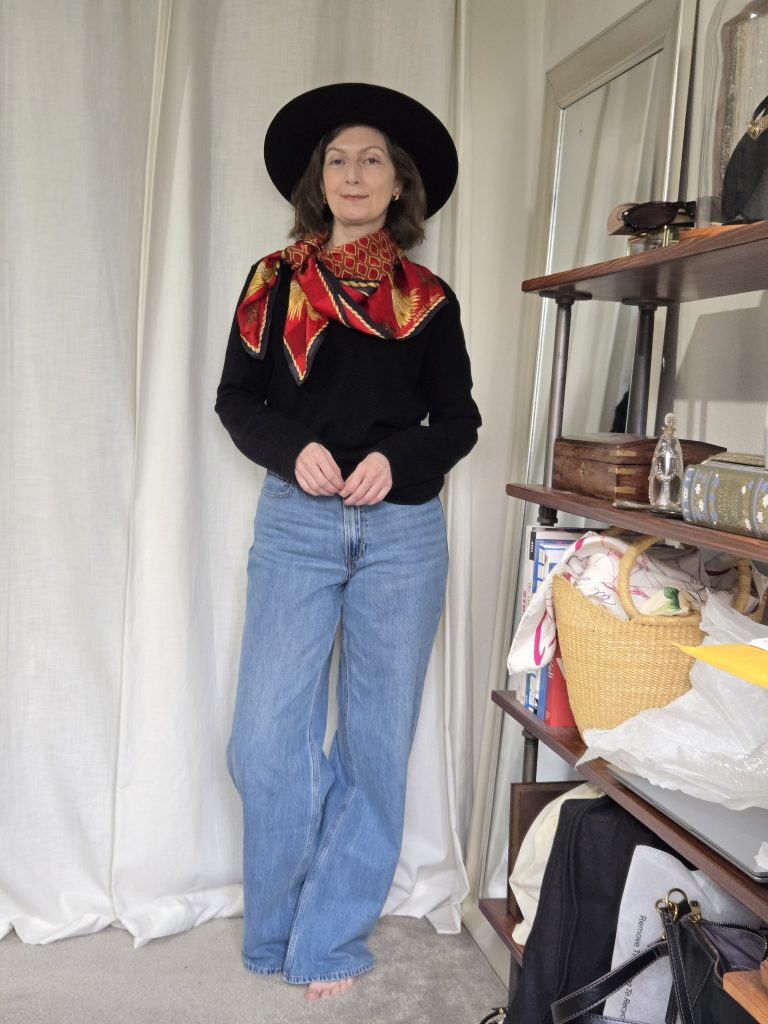 black sweater, light wash denim, red scarf and black wide brim hat